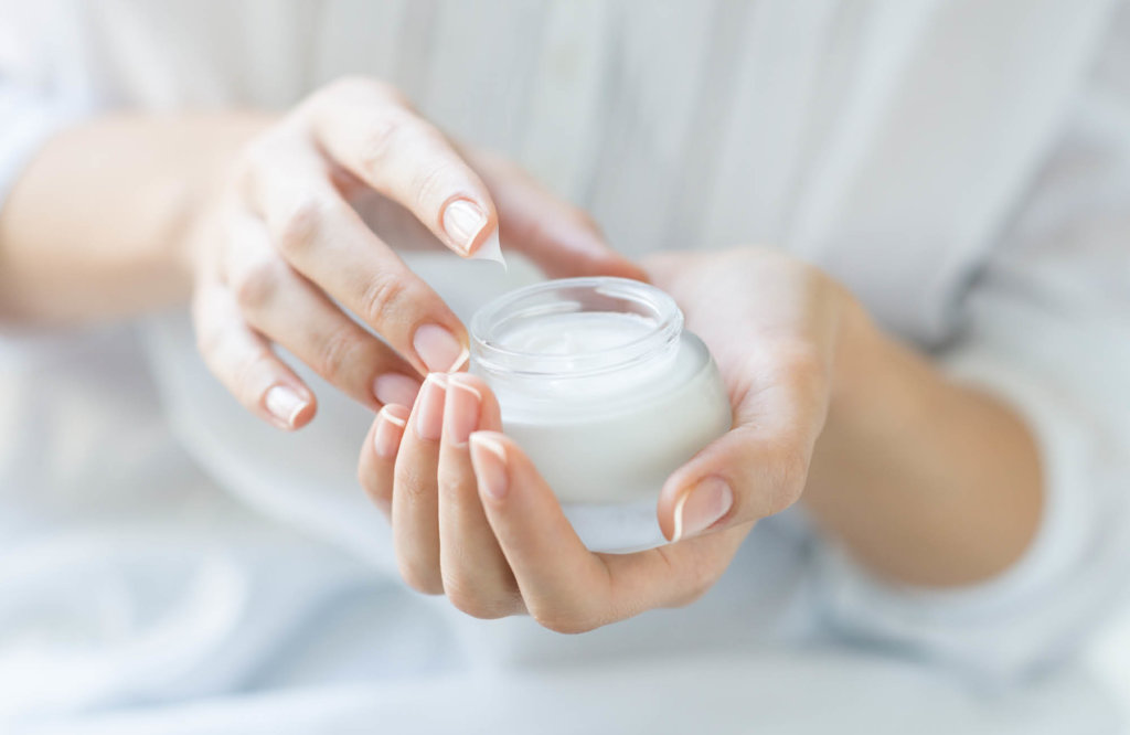 Person taking cream from the cosmetic jar