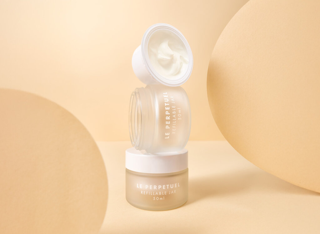 Two refillable cosmetic jars on a beige background