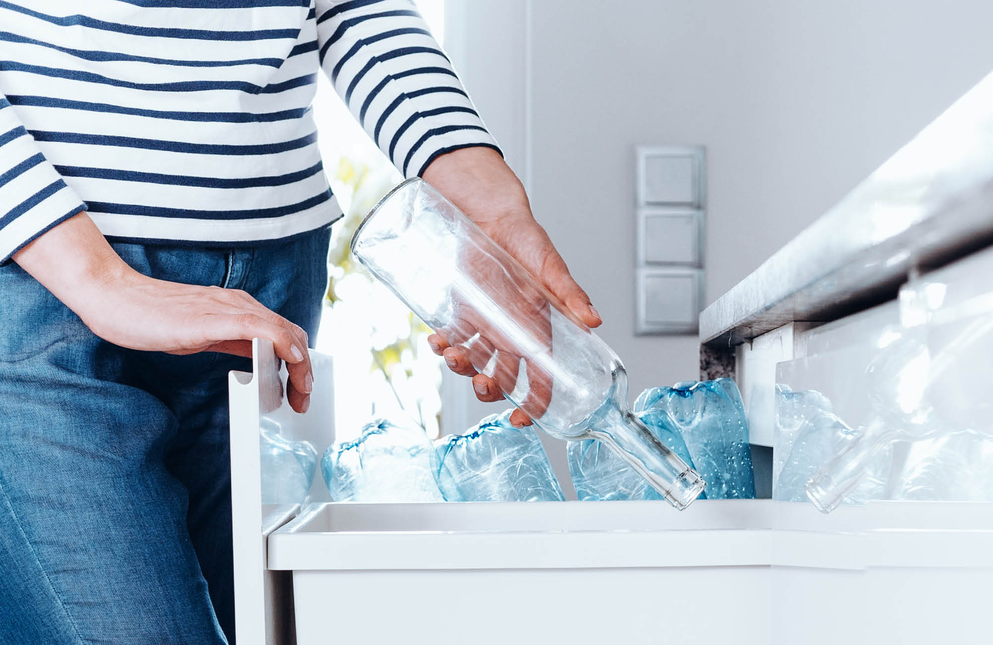 A person recycles a glass bottle in trash can of kitchen