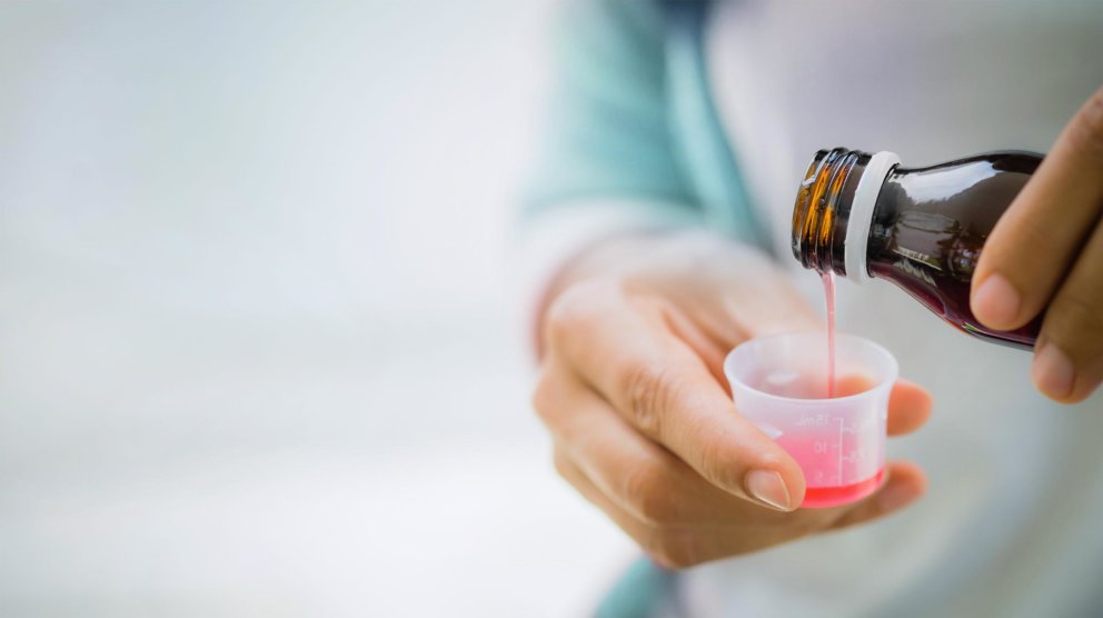 Person fills syrup from an amber bottle into the measuring cup