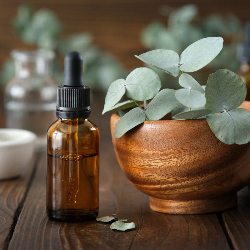 Essential oil bottle with pipette on wooden table with leafs