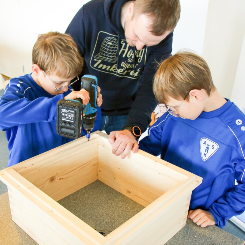 Imker und Kinder beim Bohren und Schrauben der Bienenstöcke.