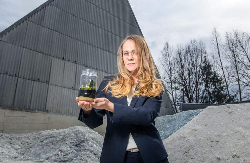 Woman holding glass jar with plants inside in front of cullet at Stoelzle site in Austria